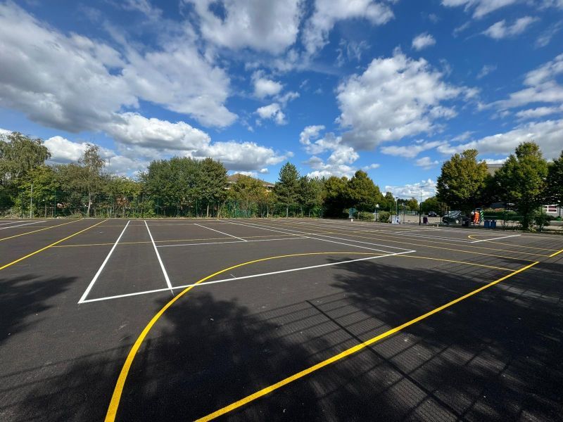 Freshly marked outdoor sports court with white court lines and yellow netball markings on tarmac by C&R
