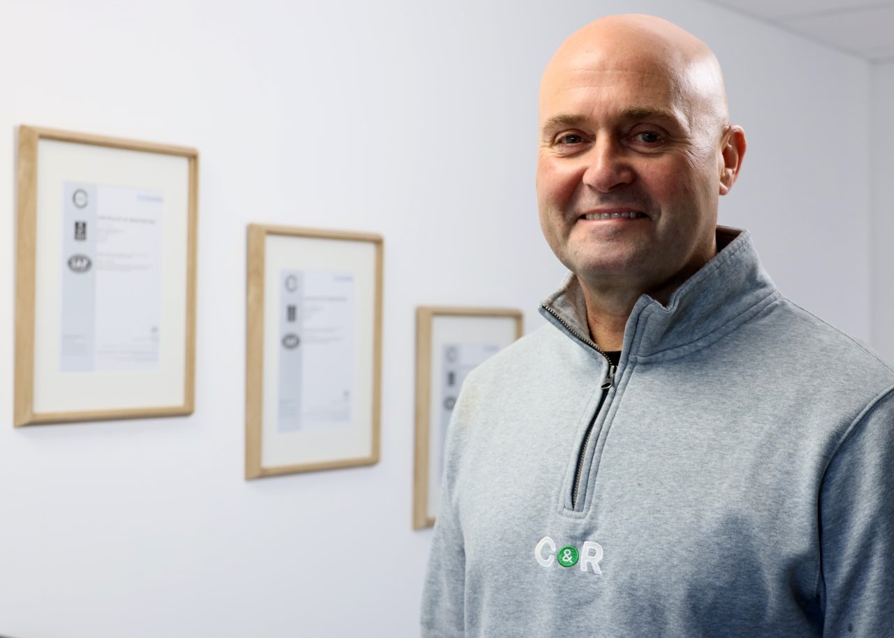 Darren Riggott, founder and Managing Director of C&R, with three framed accreditation certificates on the wall behind him